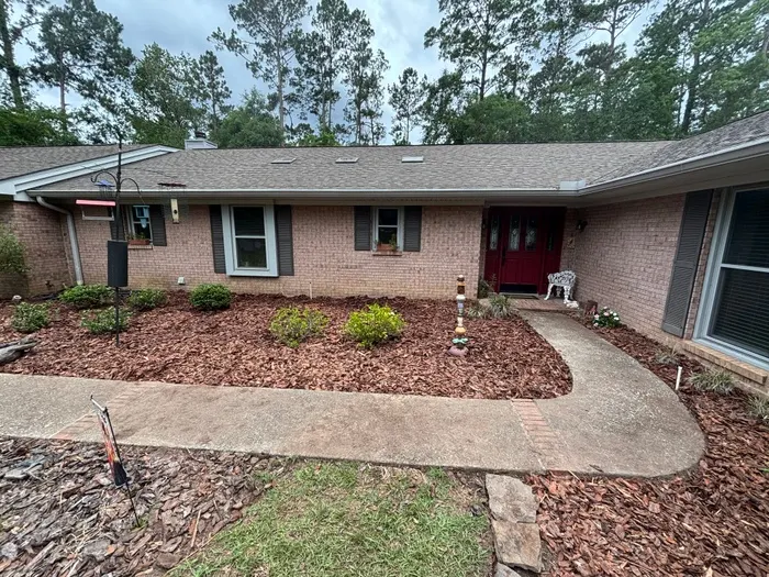 Front of a tan brick ranch with a red door, beds cleared, mulched with brown bark chips and shrubs trimmed