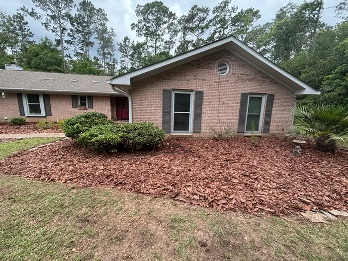 Side bed at a tan brick ranch cleared and covered with brown bark chip mulch around trimmed shrubs