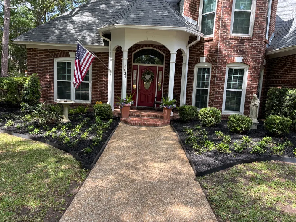 Front entry of a two-story brick home in Tallahassee, FL with black mulch beds, trimmed boxwoods and an edged walkway